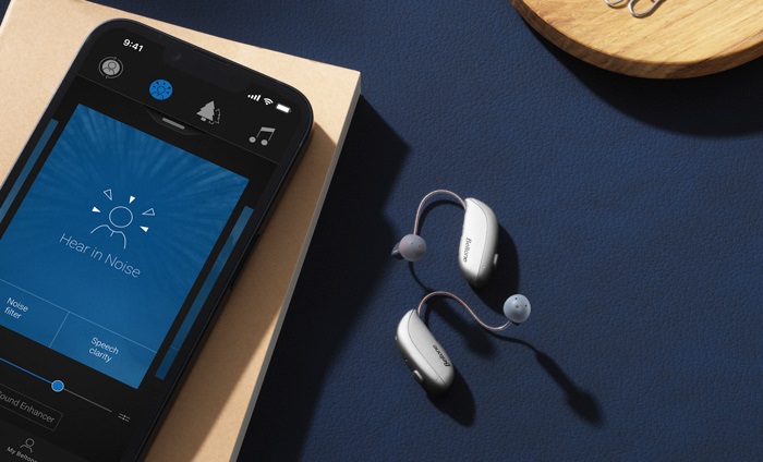 Phone open to the Beltone HearMax app with Beltone Serene hearing aids next to it